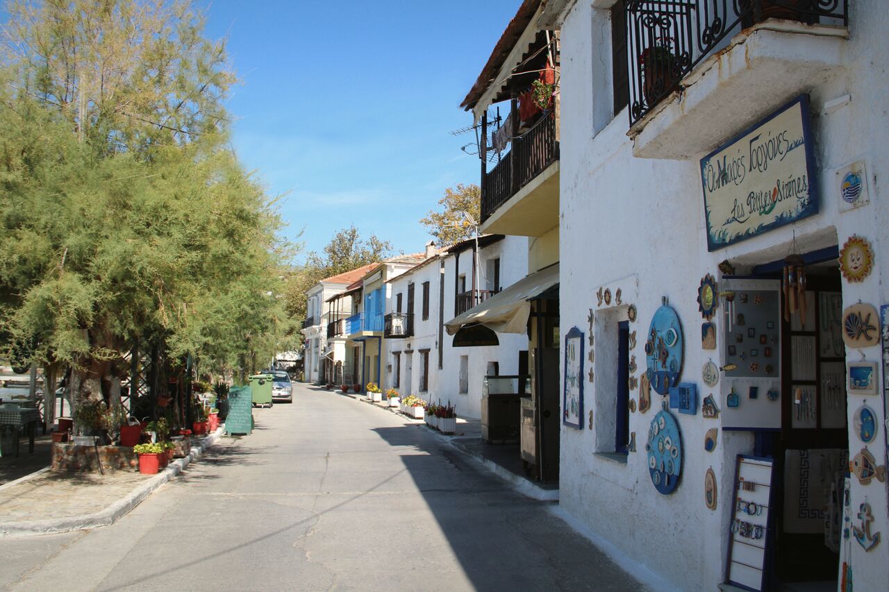 The main street of Afissos: whitewashed shopfronts with painted ceramic plates, tamarisk trees